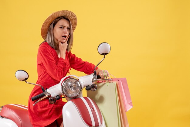 femme réfléchie en robe rouge sur cyclomoteur tenant des sacs à provisions