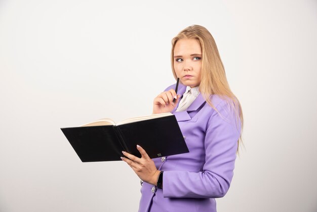 Femme réfléchie tenant une tablette ouverte sur un mur blanc.