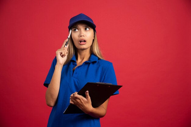 Femme réfléchie en uniforme bleu posant avec presse-papiers et crayon.