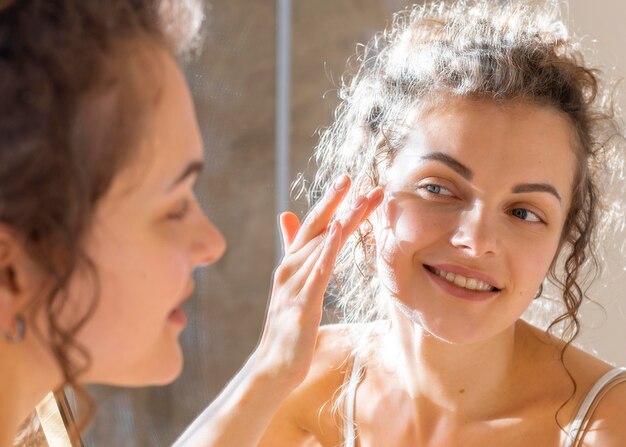 Femme regardant dans le miroir et appliquant la crème pour le visage