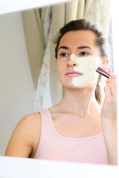 Femme regardant dans le miroir et appliquant un masque facial