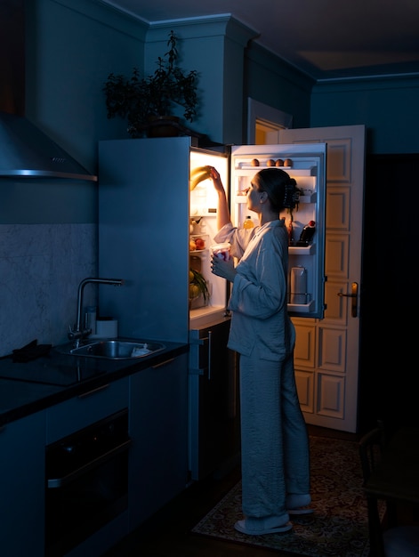 Femme regardant dans le réfrigérateur plein coup