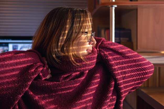 Une femme regarde à travers les stores à la lumière du soleil tôt le matin