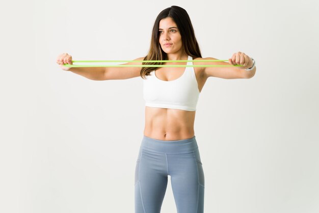 Femme de remise en forme avec un mode de vie sain à l'aide d'une bande de résistance jaune lors d'une séance d'entraînement sur un fond blanc.