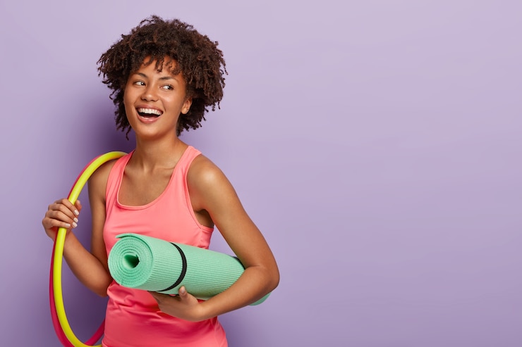 Photo gratuit femme de remise en forme à la peau foncée, travaille avec des cerceaux, tient le karemat roulé pour l'entraînement