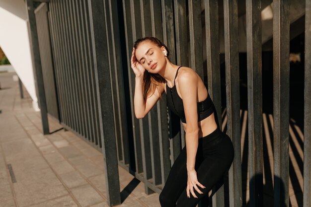 Femme de remise en forme prenant une pause après avoir exécuté une séance d'entraînement. Modèle féminin en tenue de sport exerçant à l'extérieur