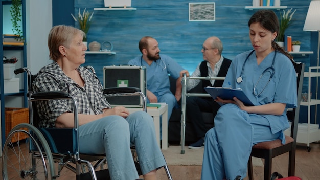 Femme retraitée handicapée parlant à une infirmière pour un examen médical dans une maison de retraite. Assistant de santé consultant un patient âgé assis en fauteuil roulant pour le soutien et l'assistance.