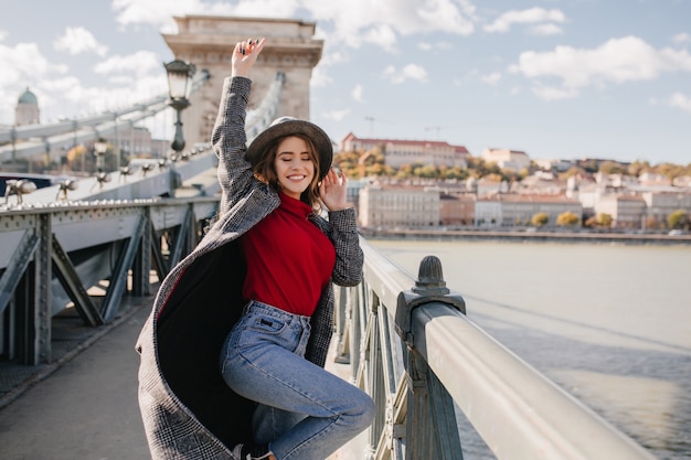 Femme rêveuse galbée posant drôle sur le pont sur fond de rivière