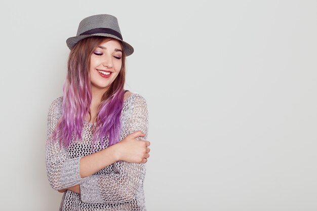 Femme rêveuse à la recherche agréable avec des cheveux violets se serrant dans ses bras et gardant les yeux fermés, exprimant le bonheur, copiez l'espace pour la publicité, isolé sur un mur blanc.