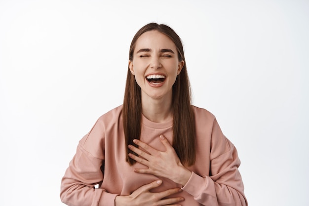 femme riant et souriant, rire de blague drôle, comédie télévisée amusante, toucher la poitrine et rire, debout sur blanc