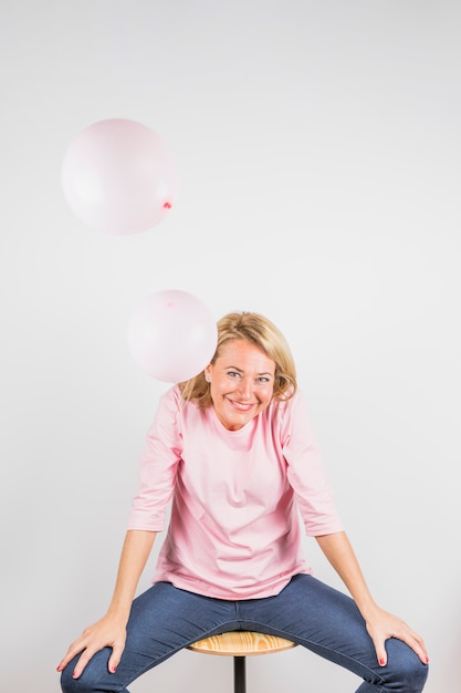 Photo gratuite femme riante âgée en chemisier rose sur un tabouret près des ballons