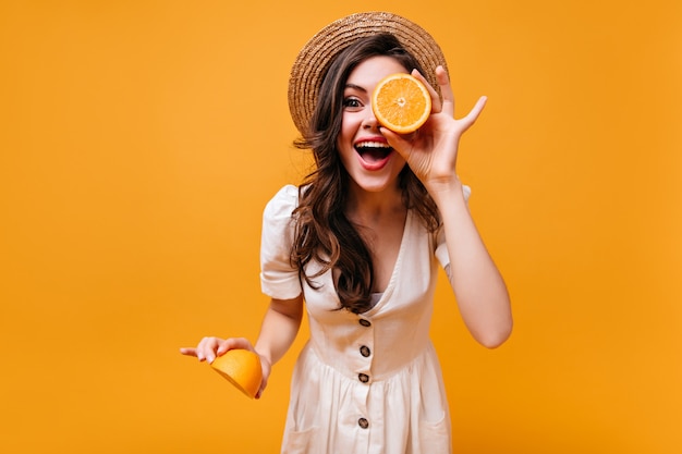 Femme en robe blanche élégante et chapeau de paille rit et détient des tranches d'oranges.