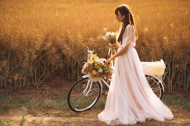 Femme en robe blanche avec vélo dans le champ