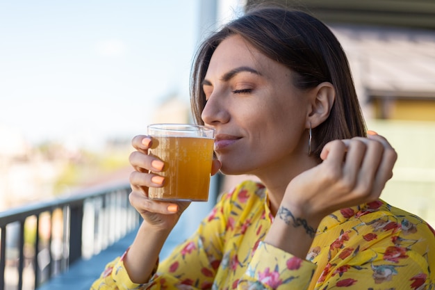 Femme en robe dans un café d'été bénéficiant d'un verre kombucha frais de bière reniflant l'odeur avec les yeux fermés