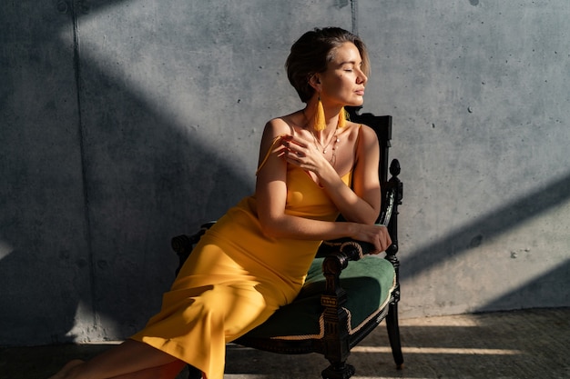 femme en robe d'été jaune avec une coiffure courte dans la chambre intérieure mur de béton posant