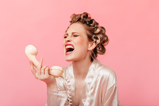 Femme en robe hurle et pleure, tenant le combiné du téléphone sur le mur rose