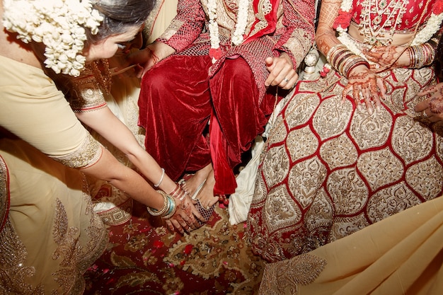 Femme en robe indienne beige se penche aux pieds du couple de mariage