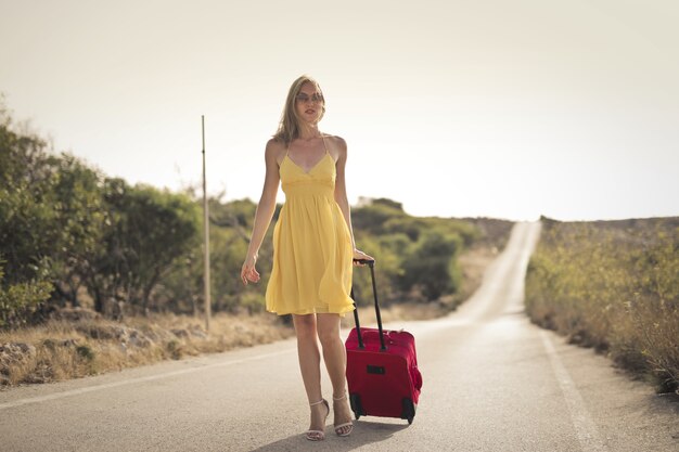 Femme avec une robe jaune et une valise rouge dans la rue