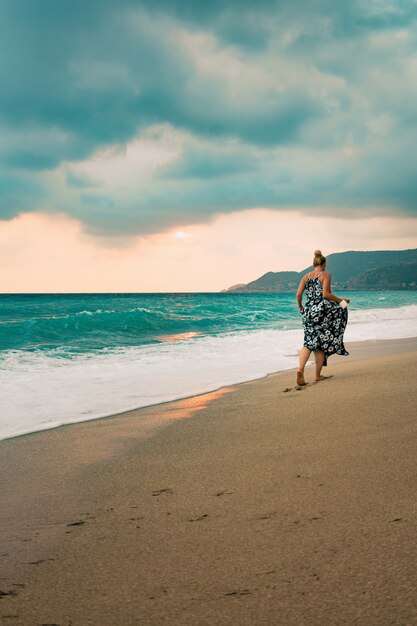 Femme en robe longue marchant au bord de la mer