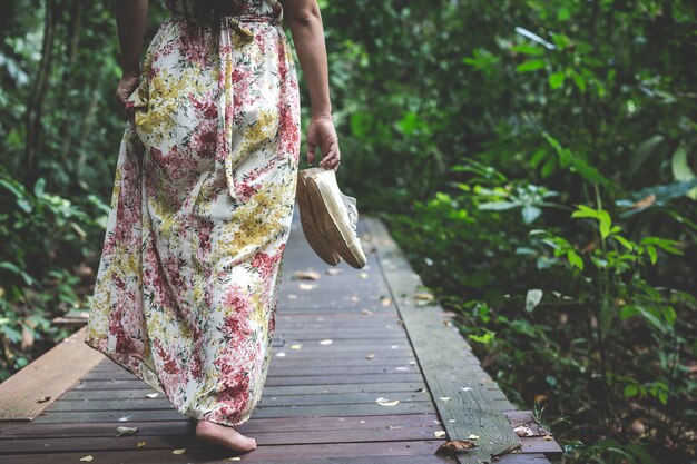 femme en robe longue porter ses chaussures marchant dans le parc