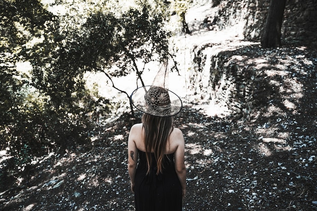 Photo gratuite femme en robe noire et chapeau debout dans la forêt