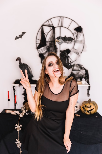 Photo gratuite femme en robe noire devant la composition d'halloween souriant et montrant la paix