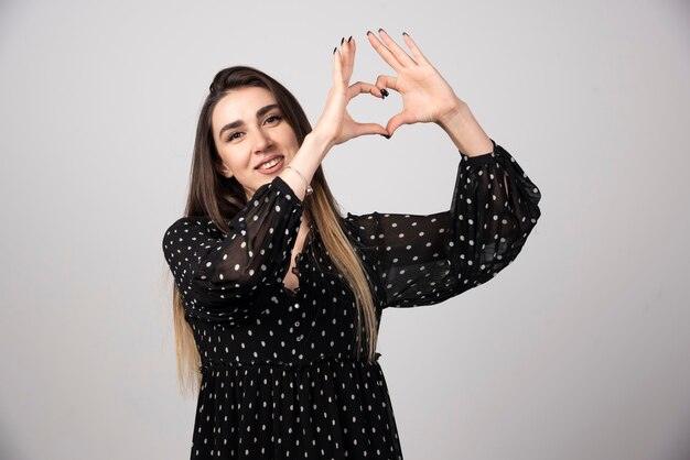 Femme en robe noire donnant le signe du coeur.