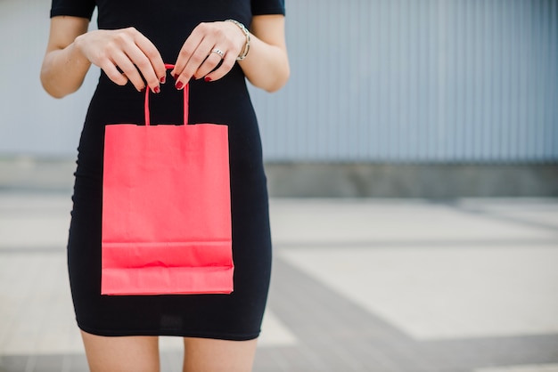 Femme en robe noire tenant un sac rouge