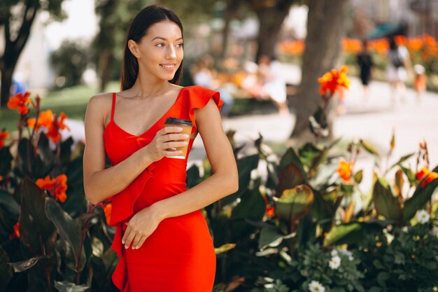 Femme en robe rouge, boire du café pour sortir dans le parc