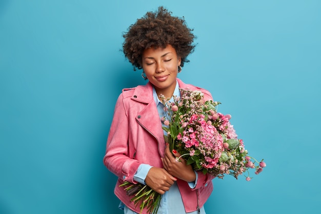 Une femme romantique heureuse reçoit un beau bouquet comme cadeau, ferme les yeux et sourit doucement, vêtue d'une veste rose