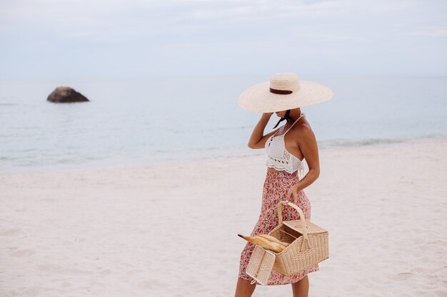 Femme romantique sur la plage en haut tricoté jupe et chapeau de paille tenant panier avec pain Eco life