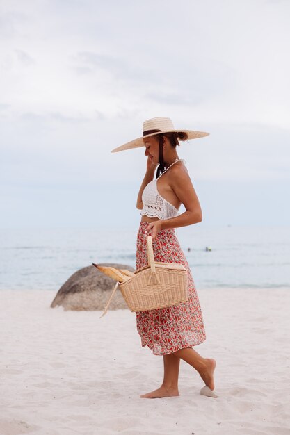 Femme romantique sur la plage en haut tricoté jupe et chapeau de paille tenant panier avec pain Eco life