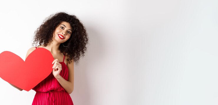 Photo gratuit femme romantique en robe montrant un grand coeur rouge tombant amoureux souriant heureux à l'arrière-plan blanc de l'appareil photo