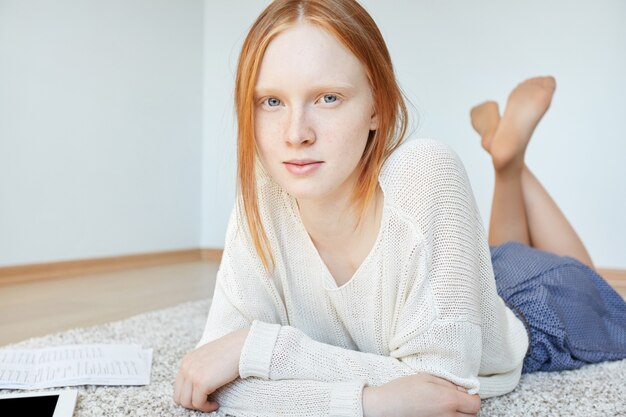 Femme rousse allongée sur le sol avec ordinateur portable et tablette