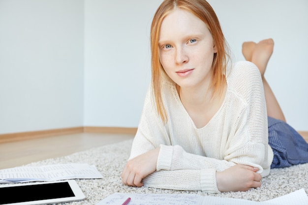 Femme rousse allongée sur le sol avec ordinateur portable et tablette