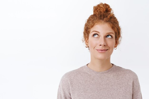 femme rousse aux cheveux bouclés peignés en chignon désordonné, souriant sur blanc