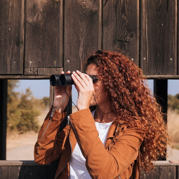 Femme rousse bouclée regardant à travers des jumelles