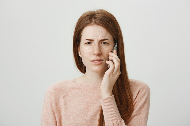 Femme rousse confuse fronçant les sourcils perplexe comme parler au téléphone mobile