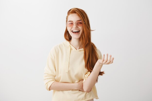 Femme rousse élégante à lunettes de soleil en riant et souriant heureux