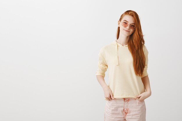 Femme rousse élégante souriante à lunettes de soleil debout