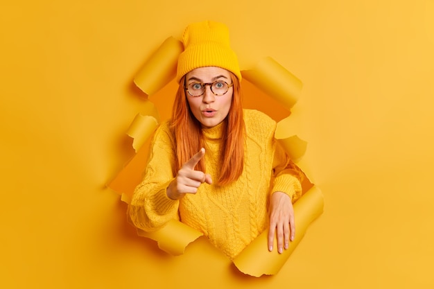 Une femme rousse étonnée montre avec une expression surprise que quelqu'un voit quelque chose d'incroyable devant.