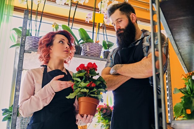 Femme rousse et homme tatoué barbu vendant des fleurs dans un magasin du marché.