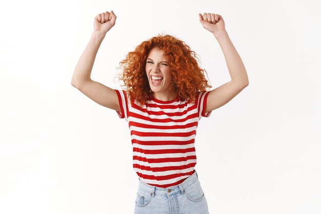 Femme rousse insouciante et insouciante aux cheveux bouclés sautant danser s'amusant à crier chanter le long du concert du groupe de musique lever les mains victoire triomphe geste crier ouais