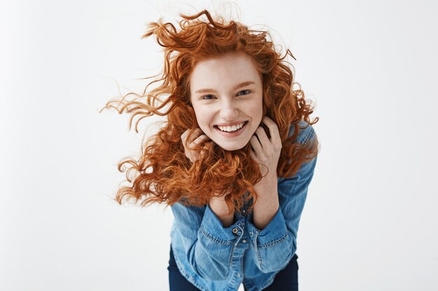 femme rousse joyeuse avec des cheveux bouclés volants souriant en riant.