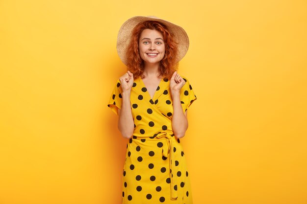 femme rousse joyeuse posant en robe à pois jaune et chapeau de paille