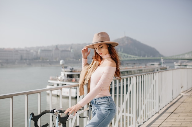 Photo gratuite femme rousse pensif en chapeau posant sur le mur du ciel en week-end