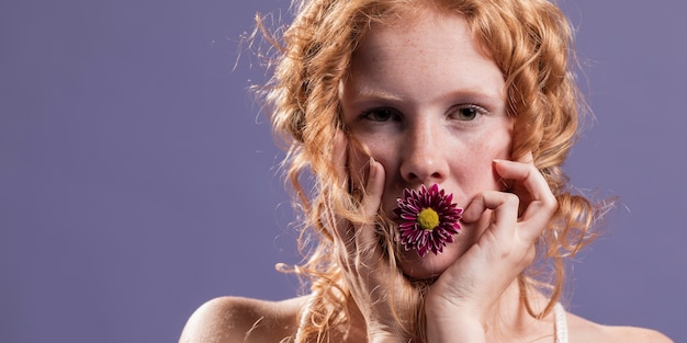 Femme rousse posant avec un chrysanthème sur sa bouche et copie espace