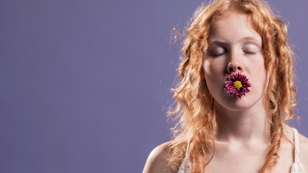 Femme rousse posant avec une fleur sur sa bouche et copie espace