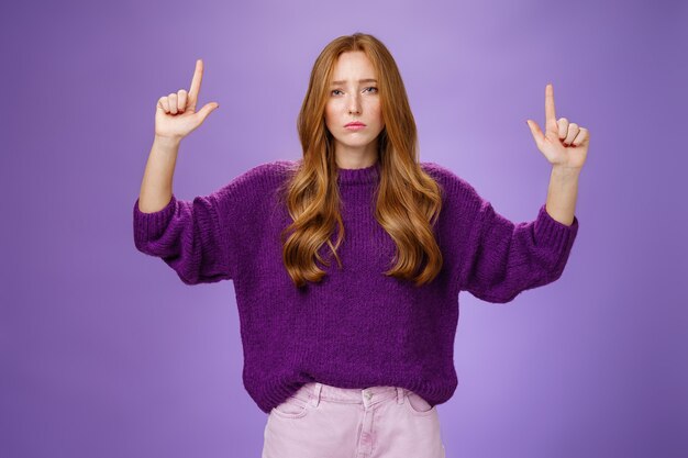 Femme rousse séduisante, triste et de mauvaise humeur, avec des taches de rousseur dans un pull chaud, levant les mains p ...