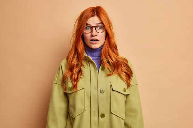 La femme rousse surprise regarde avec émerveillement retient son souffle de stupéfaction ne peut pas croire à une révélation choquante vêtue d'un manteau vert.